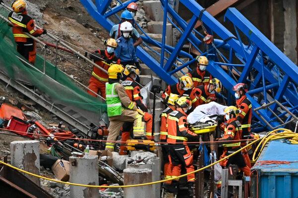 An injured person was trapped underneath the crane, only his lower body was visible until evening. He was rescued, covered with white sheet, and carried from the scene by firefighters. (Sung Pi-Lung/The Epoch Times)
