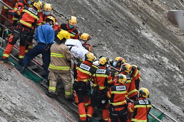 An injured person, who was trapped underneath the crane, was rescued and carried from the scene by firefighters. (Sung Pi-Lung/The Epoch Times)