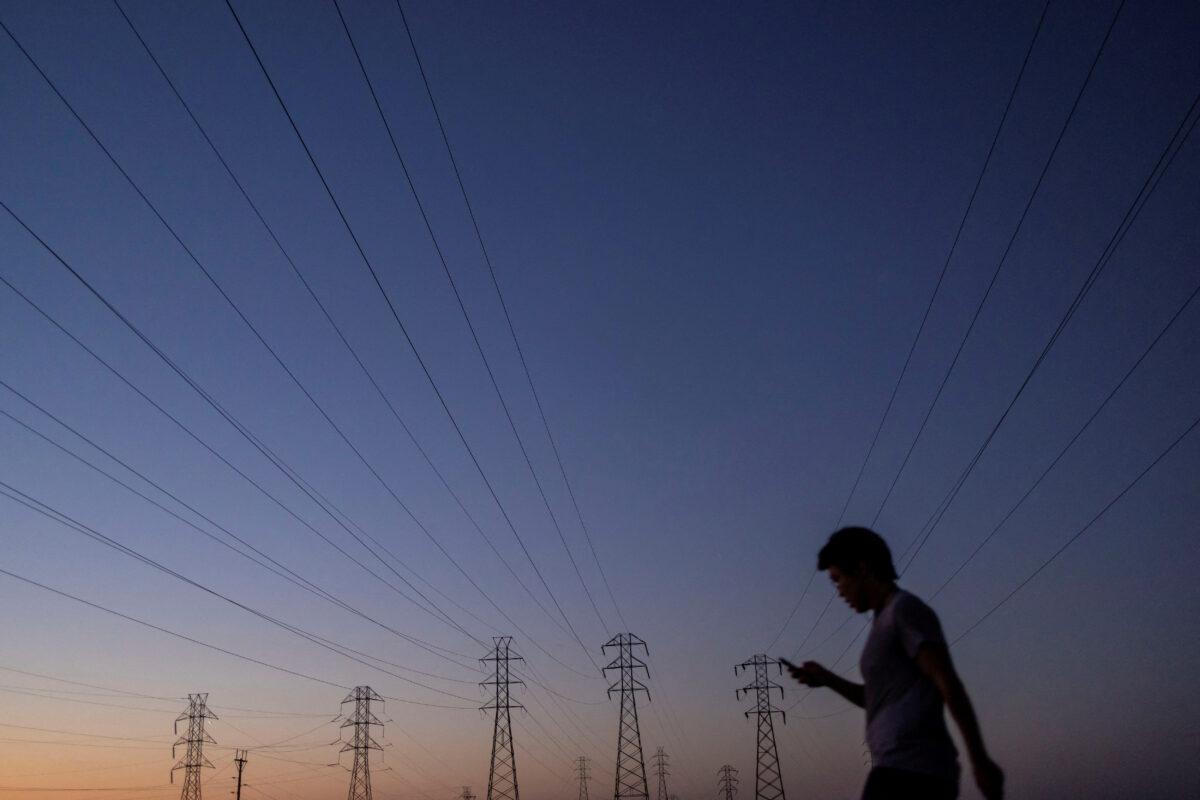 A man walks by power lines as California’s grid operator urged the state’s 40 million people to ratchet down the use of electricity in homes and businesses as a heat wave settled over much of the state, in Mountain View, Calif., on Aug. 17, 2022. (Carlos Barria/Reuters)
