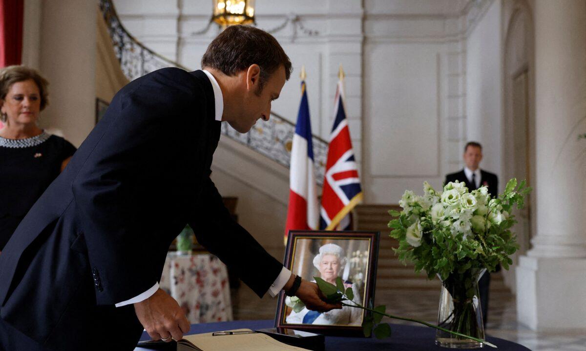 French President Emmanuel Macron places a white rose next to a portrait of Queen Elizabeth II, after signing the condolence book at the British Embassy in Paris on Sept. 9, 2022 (Christian Hartmann/Pool/AFP via Getty Images)