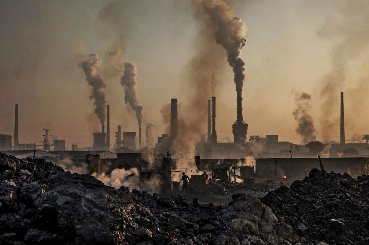 Smoke billows from a large steel plant as a Chinese labourer works at an unauthorized steel factory, foreground, on November 4, 2016 in Inner Mongolia, China. (Kevin Frayer/Getty Images)