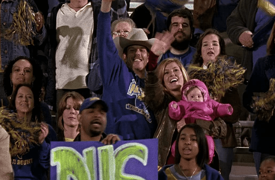 Dillon High principal Tami Taylor (Connie Britton) holds baby Grace (in pink) and celebrates a game with an old flame played by "Friday Night Lights" director Peter Berg (in cowboy hat), in "Friday Night Lights." (Universal Television)