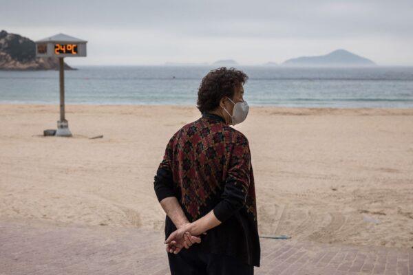 A woman watches as workers put up a fence to block access to Shek O beach in Hong Kong on March 17, 2022, after the government said it would close public beaches to curb the spread of the new coronavirus. (Dale De La Rey/AFP via Getty Images)