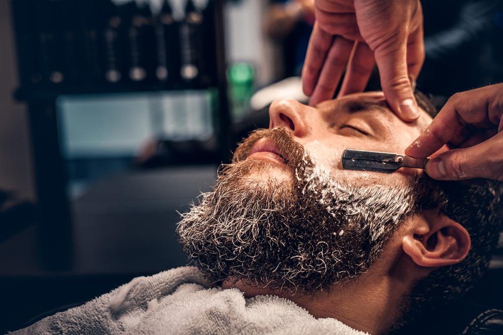 If you’re a bit hesitant to try shaving with a straight razor, which is understandable, consider getting a barbershop shave to see how a pro wields the blade. (FXQuadro/Shutterstock)