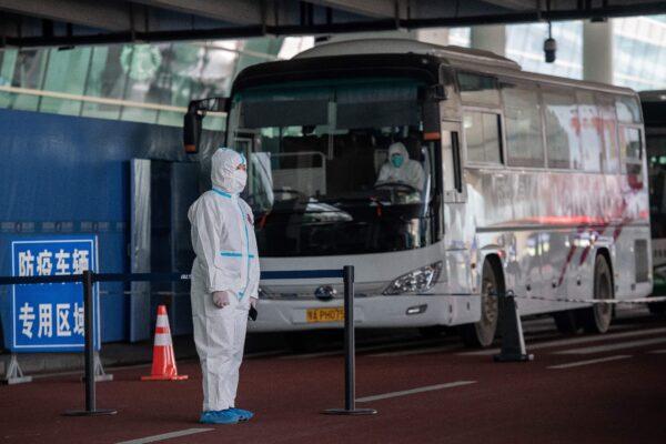 A health worker wearing a personal protection suit stands next to buses at a cordoned-off section at the international arrivals area, where arriving travelers are to be taken into quarantine, at the international airport in Wuhan, China, on Jan. 14, 2021. (Nicolas Asfouri/AFP via Getty Images)