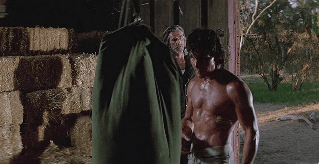 Dalton (Patrick Swayze, foreground) lets off some steam with a make-shift heavy bag as his mentor and buddy Wade Garrett (Sam Elliott) watches, in "Road House." (United Artists)