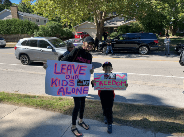 A local mother and her child protest outside Oakville Trafalgar High School on Sept. 23. against a teacher wearing large prosthetic breasts to class. (The Epoch Times/Peter Wilson)