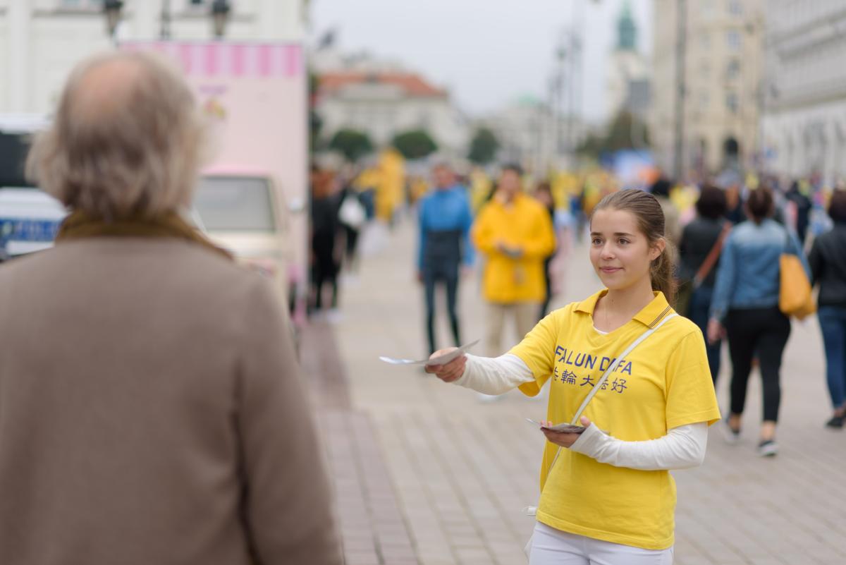 A girl hands out flyers during a march held by Falun Dafa practitioners through the center of Warsaw, Poland, on Sept. 9, 2022. (Mihut Savu/The Epoch Times)