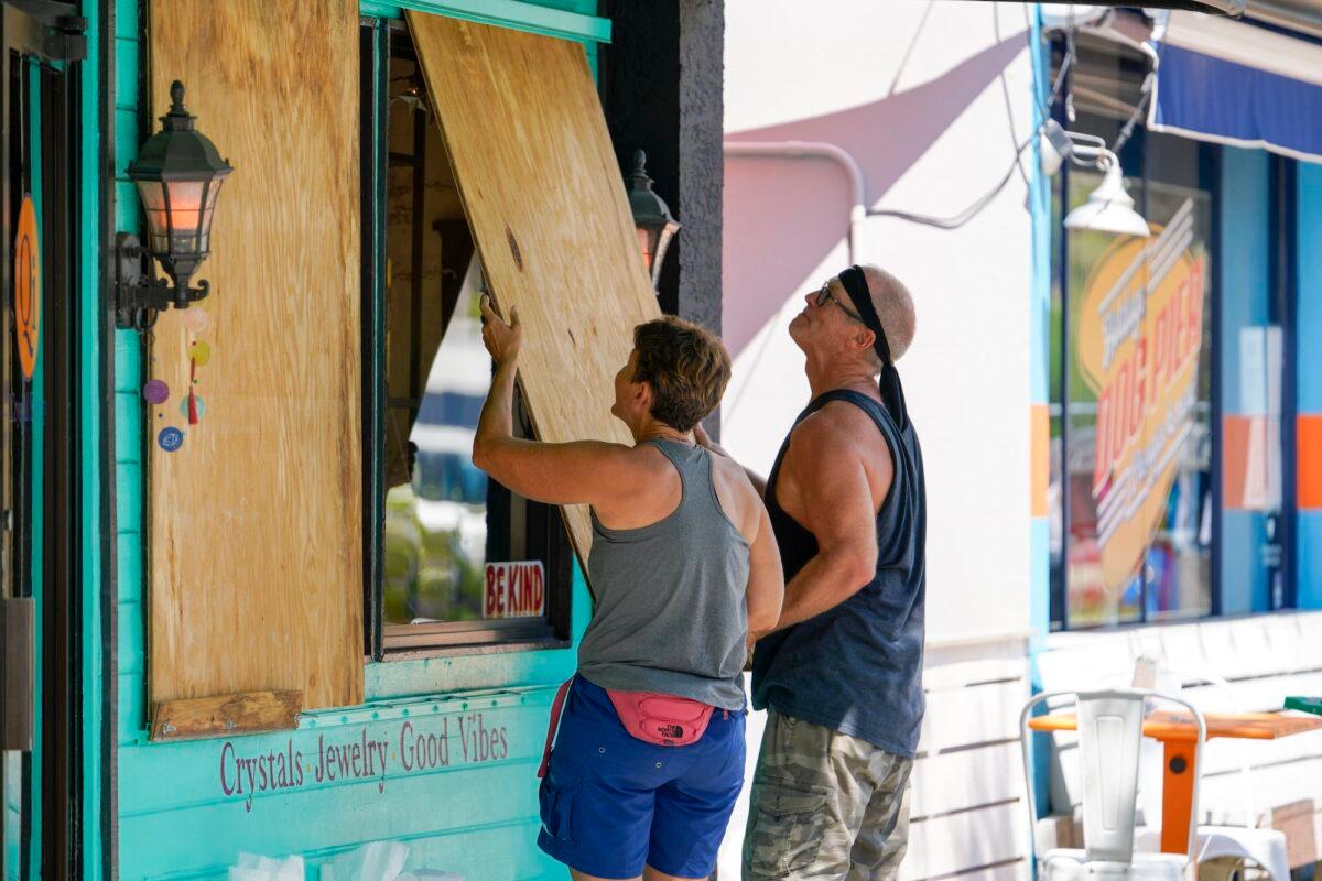 Lisa Bromfield and Mike Sernett work to place a sheet of plywood on the front windows of a store in downtown Gulfport in preparation for the arrival of Hurricane Ian, in South Pasadena, Fla., on Sept. 26, 2022. (Martha Asencio-Rhine/Tampa Bay Times via AP)