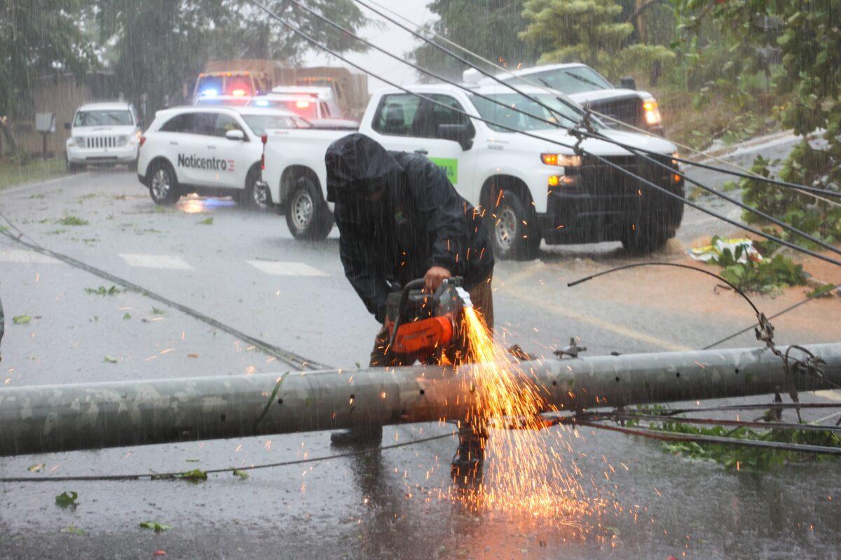A worker cuts an electricity pole that was downed by Hurricane Fiona as it blocks a road in Cayey, Puerto Rico, on Sept. 18, 2022. (Stephanie Rojas/AP Photo)