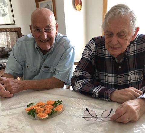 The author's husband, Joe Fisher (L), and Paul Muller enjoy a snack of 'Iowa salmon' on party crackers. (Courtesy of Kay E. Fisher)