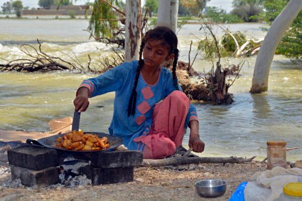 A displaced girl cooks potatoes next to floodwaters after taking refuge from her family's flood-hit home, in Multan, Pakistan, on Aug. 31, 2022. (Shazia Bhatti/AP Photo)