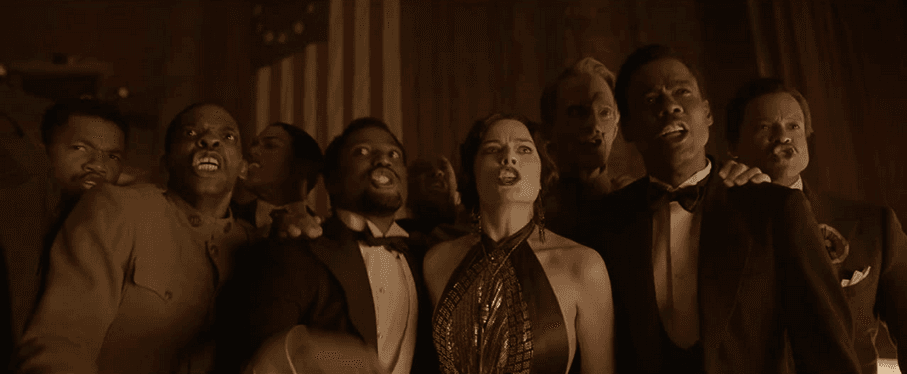 (L–R, foreground, starting second from left) John David Washington, Margot Robbie, and Chris Rock boo a small faction of proto-Nazis at a function for veterans in 1930s New York, in "Amsterdam." (20th Century Studios)