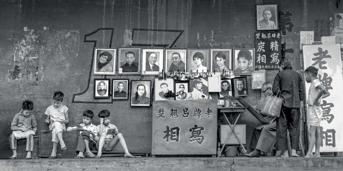 On the streets of Wong Tai Sin, skilled painters copy people's small photos. Their painting skills were so good that people would confuse their works with real photos. Stall owners would also rent comic books to children, which is captured in this street scene. (Courtesy of Eastpro Gallery)