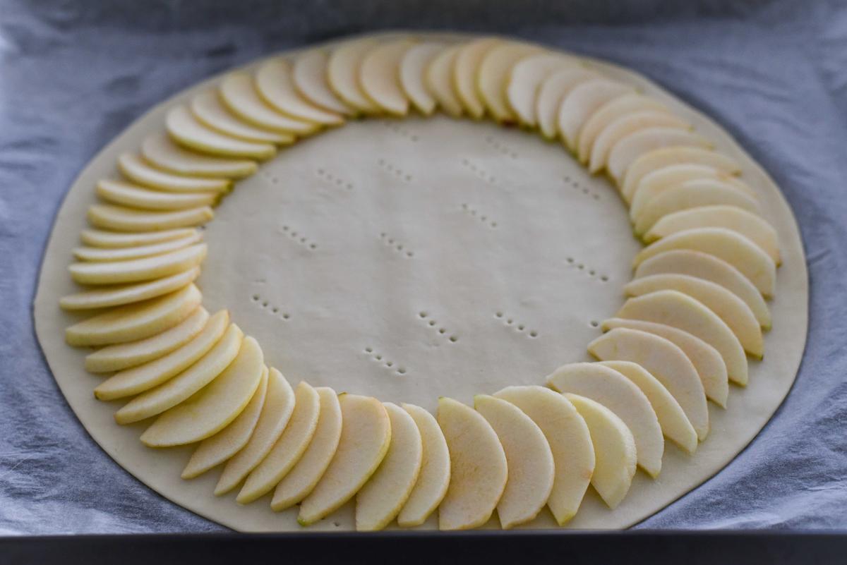 Starting with the larger slices, working from the outer edges to the center, arrange the apple slices on the puff pastry circle in slightly overlapping rings. (Audrey Le Goff)