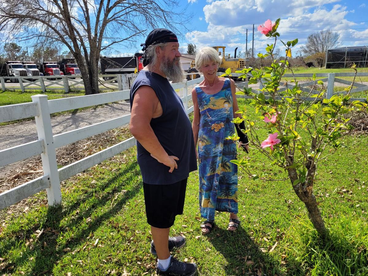 New Florida residents Ross and Rita Davis marvel at the flowers remaining on a bush in their Punta Gorda, Fla., yard on Oct. 5, 2022, a week after deadly Hurricane Ian roared through. The plant is a symbol of "renewed hope," they say. (Jann Falkenstern/The Epoch Times)