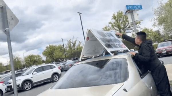 Two Chinese men are seen graffitiing signage on a car that reads “End the evil CCP (Chinese Communist Party)" at Floriade car park in Canberra, Australia, on Oct. 4, 2022. (Supplied)