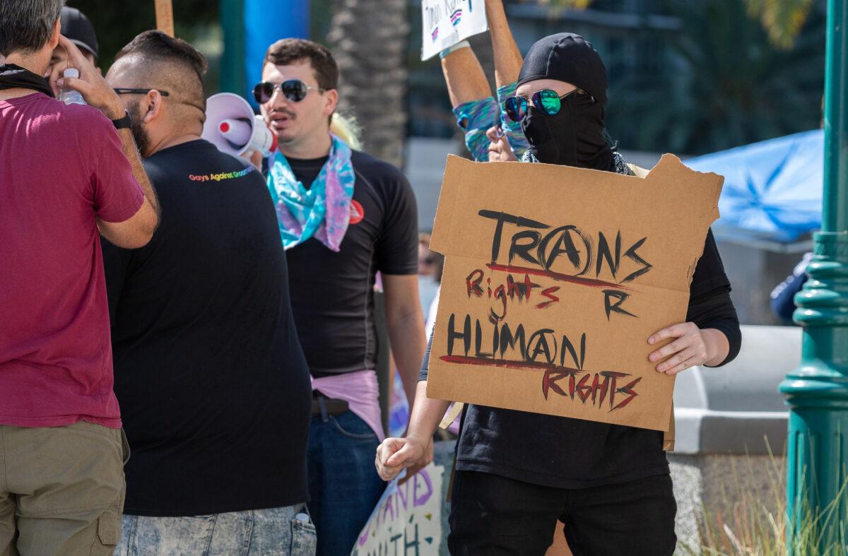 A transgender activist wearing all black stands near detransition demonstrators in Anaheim, Calif., on Oct. 8, 2022. (John Fredricks/The Epoch Times)