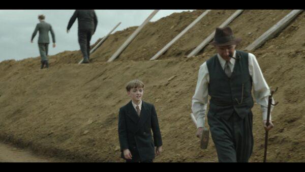 Edith Pretty's son, Robert (Archie Barnes, L), follows archaeologist-excavator Basil Brown (Ralph Fiennes) in search of a fabulous archeological find in the English countryside. (Netflix)