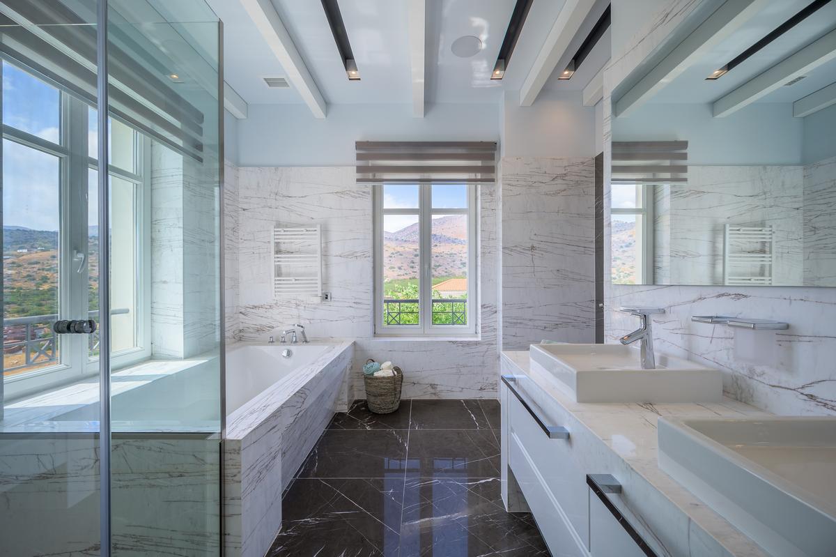 This bathroom features a sleek, modern design with expansive windows to enjoy the gorgeous views in every direction. (Courtesy of Greece Sotheby's International Realty)