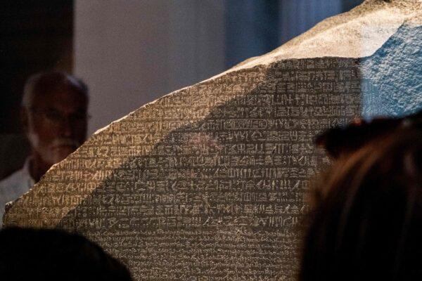 Visitors view the Rosetta stone at the British Museum in London on July 26, 2022. The Rosetta stone—a basalt slab dating from 196 B.C., which bore extracts of a decree written in ancient Greek, an ancient Egyptian vernacular script called demotic, and hieroglyphics—has been housed in the British Museum since 1802. (Amir Makar/AFP via Getty Images)