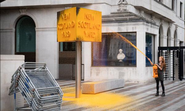 A Just Stop Oil protester spray paints a sign outside New Scotland Yard in London on Oct. 14, 2022. (Stefan Rousseau/PA Media)