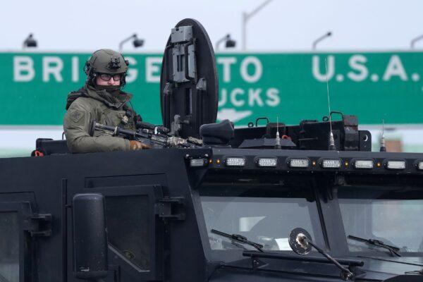 An Ontario Provincial Police tactical officer looks on from the top hatch of an armoured vehicle as demonstrators prepare to leave in advance of police enforcing an injunction against their demonstration at the Ambassador Bridge in Windsor, Ont., on Feb. 12, 2022. (The Canadian Press/Nathan Denette)
