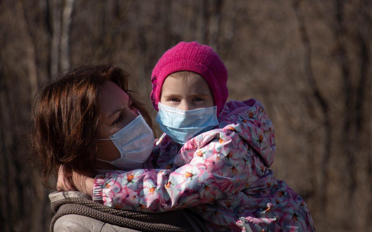 A mom holds her daughter, both wearing masks, during the COVID-19 pandemic, in a file photo. (Nik Anderson/Flickr, CC BY 2.0)