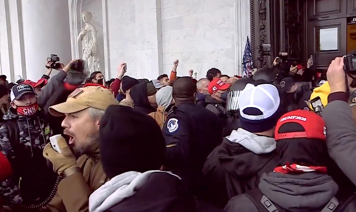 Retired police sergeant and Oath Keeper Michael Nichols uses a bullhorn to ask people to make way for the police officers they were extracting from the Capitol on Jan. 6, 2021. Directly behind him is Capitol Police Lt. Tarik Johnson. (U.S. DOJ/Screenshot via The Epoch Times)