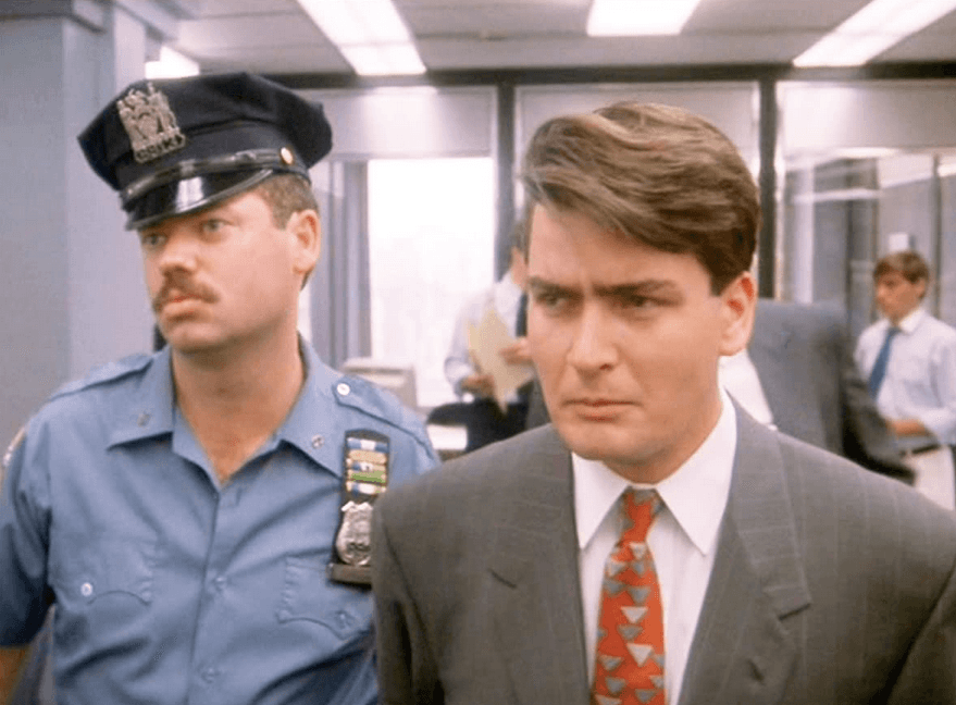 Bud Fox (Charlie Sheen, R), doing a handcuffed walk of shame through his office, is off to jail on federal charges of securities fraud, in "Wall Street." (20th Century Fox)