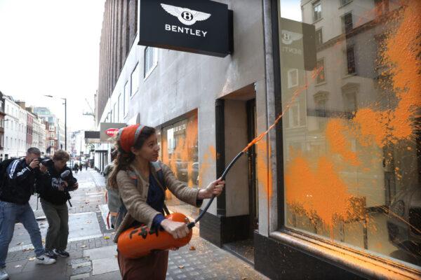 A demonstrator from Just Stop Oil sprays an orange substance on the Jack Barclay Bentley store in Berkeley Square, in London, England, on Oct. 26, 2022. (Isabel Infantes/Getty Images)