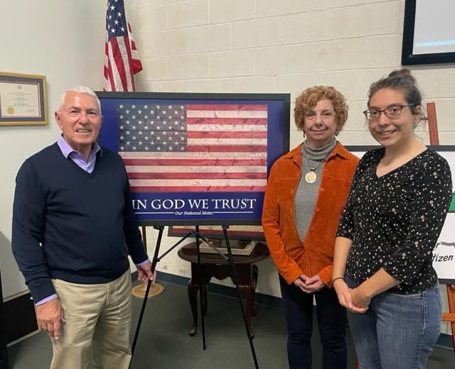 EmpowerU America board members, John O’Neill (L), Nita Thomas (2R) and Leigh Ann Cartier (R), pose with one of four posters that donors can purchase for display in an Ohio school district to promote the national motto, "In God. We Trust," in October 2022. (Courtesy of Dan Regenold)