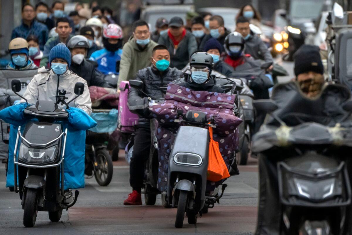 Commuters wearing masks ride scooters along a street in the central business district in Beijing on Oct. 28, 2022. (Mark Schiefelbein/AP Photo)