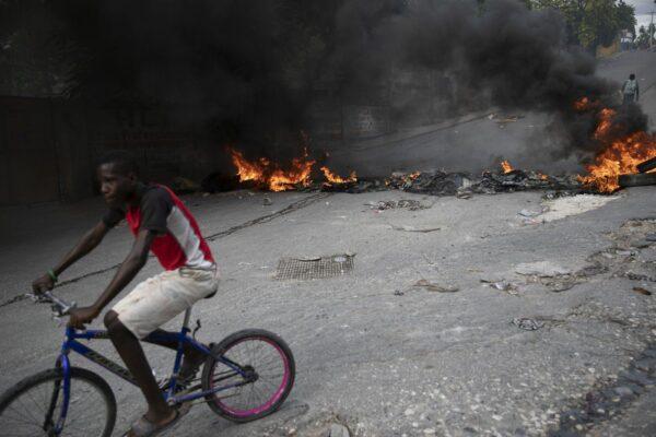 A man rides his bicycle past a burning barricade during a protest over the death of journalist Romelo Vilsaint, in Port-au-Prince, Haiti, Oct. 30, 2022. (The Canadian Press/Odelyn Joseph)