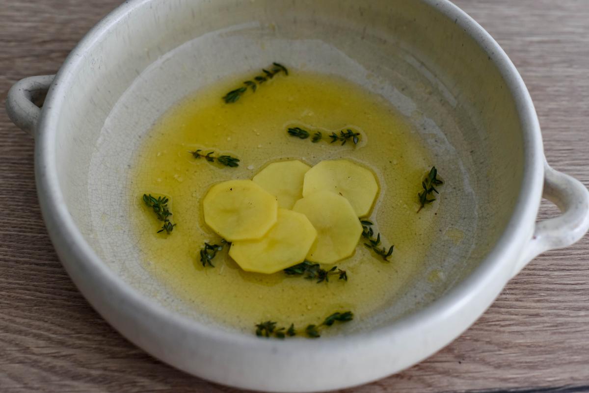 Pour half of the clarified butter on the bottom of your skillet or dish, scatter with thyme, and begin arranging the potato slices in an overlapping spiral pattern. (Audrey Le Goff)