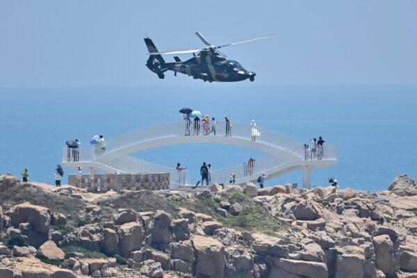 Tourists look on as a Chinese military helicopter flies past Pingtan island, one of mainland China's closest point from Taiwan, in Fujian province on August 4, 2022. (HECTOR RETAMAL/AFP via Getty Images)