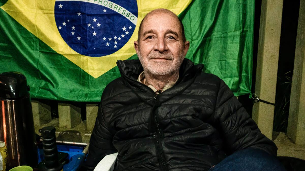 Luiz Henrique poses for a photograph in front of a Brazilian flag he hung next to his family’s tent in Curitiba, Brazil, on Nov. 4, 2022. (Frederico Vidovix/The Epoch Times)