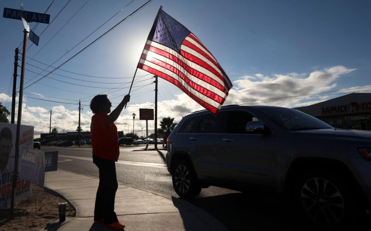 A woman waves an American flag to greet motorists as they head to vote in the U.S. midterm election at The Cesar Chavez Cultural Center in San Luis, Ariz., on Nov. 8, 2022. (Sandy Huffaker/AFP via Getty Images)