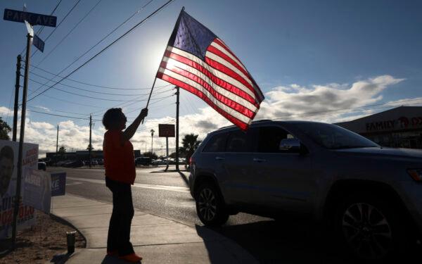 A woman waves an American flag to greet motorists as they head to vote in the U.S. midterm election at The Cesar Chavez Cultural Center in San Luis, Arizona, on Nov. 8, 2022. (Sandy Huffaker/AFP via Getty Images)