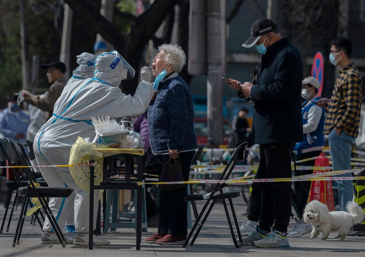 A health worker wears protective gear as she takes a throat swab for nucleic acid testing to detect COVID-19 at a mass testing site after new cases were found in the area on April 6, 2022, in Beijing, China. (Kevin Frayer/Getty Images)