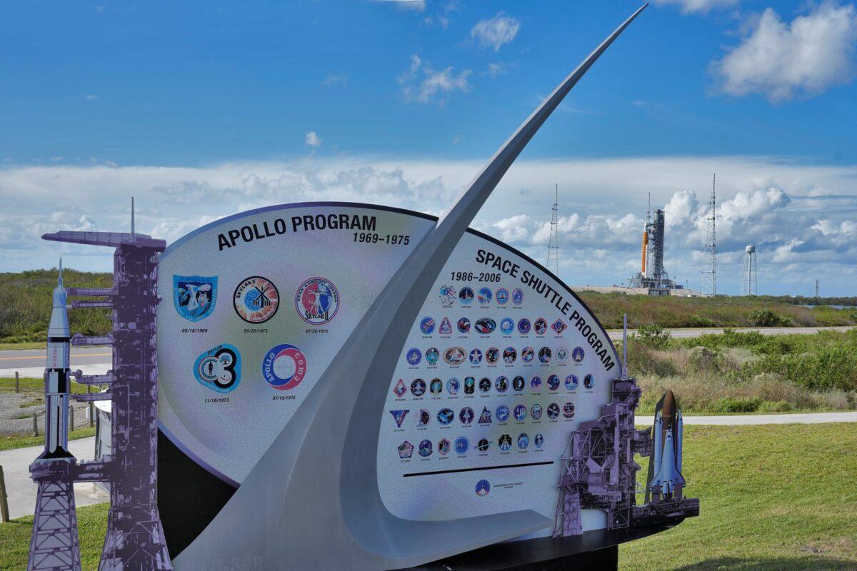 A sign showing NASA's Apollo and Space Shuttle programs near NASA's new moon rocket as she sits on Launch Pad 39-B in Cape Canaveral, Fla., on Nov. 11, 2022. (Chris O'Meara/AP Photo)