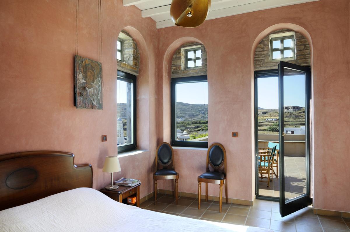 The bedroom in the upper-level guest quarters uses large windows to provide a wonderful view of the surrounding countryside, with an even better view from the adjacent terrace. (Courtesy of Greece Sotheby’s International Realty)