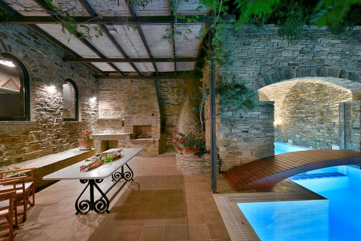 Adjacent to the partially-covered pool and its delightful bridge, is an alfresco dining area equipped with a stone oven for relaxed family meals or entertaining guests. (Courtesy of Greece Sotheby’s International Realty)
