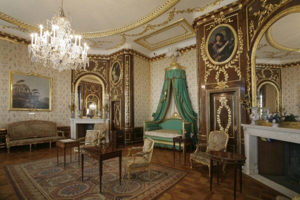 The walls of the Royal Bedroom are lined in cream silk with floral patterns and yew paneling with gilded laurel branches, both complementing the Carrara marble fireplace. The Turkish-style bed in duck egg green is a reconstruction of the one that the king sat on during the day and slept upright in during the night. Paintings by Italian Marcello Bacciarelli show scenes from the Old Testament, and the couches and armchairs are upholstered in tapestries of Jean de la Fontaine's fables. (A. Ring/Royal Castle in Warsaw)