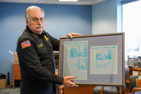 Orange County Sheriff Carl DuBois holds a newspaper frame that displays news articles about the change he made as a new sheriff in the early 2000s in his office in Goshen, N.Y., on Nov. 19, 2022. (Cara Ding/The Epoch Times)