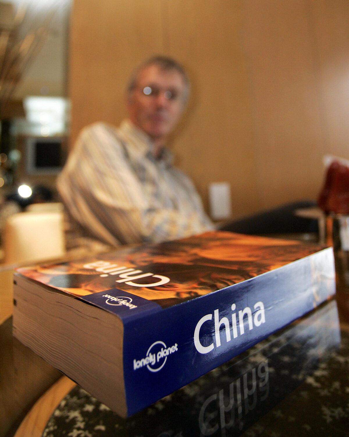 A "Lonely Planet" travel book rests on a coffee table while in the background is the book's founder Tony Wheeler in Hong Kong on Sept. 23, 2006. (Laurent Fievt/AFP via Getty Images)