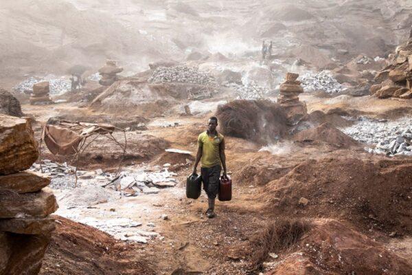 A man carries drums of water through Pissy Granite Mine in the centre of Ouagadougou, Burkina Faso, on Jan. 29, 2022. (John Wessels/AFP via Getty Images)