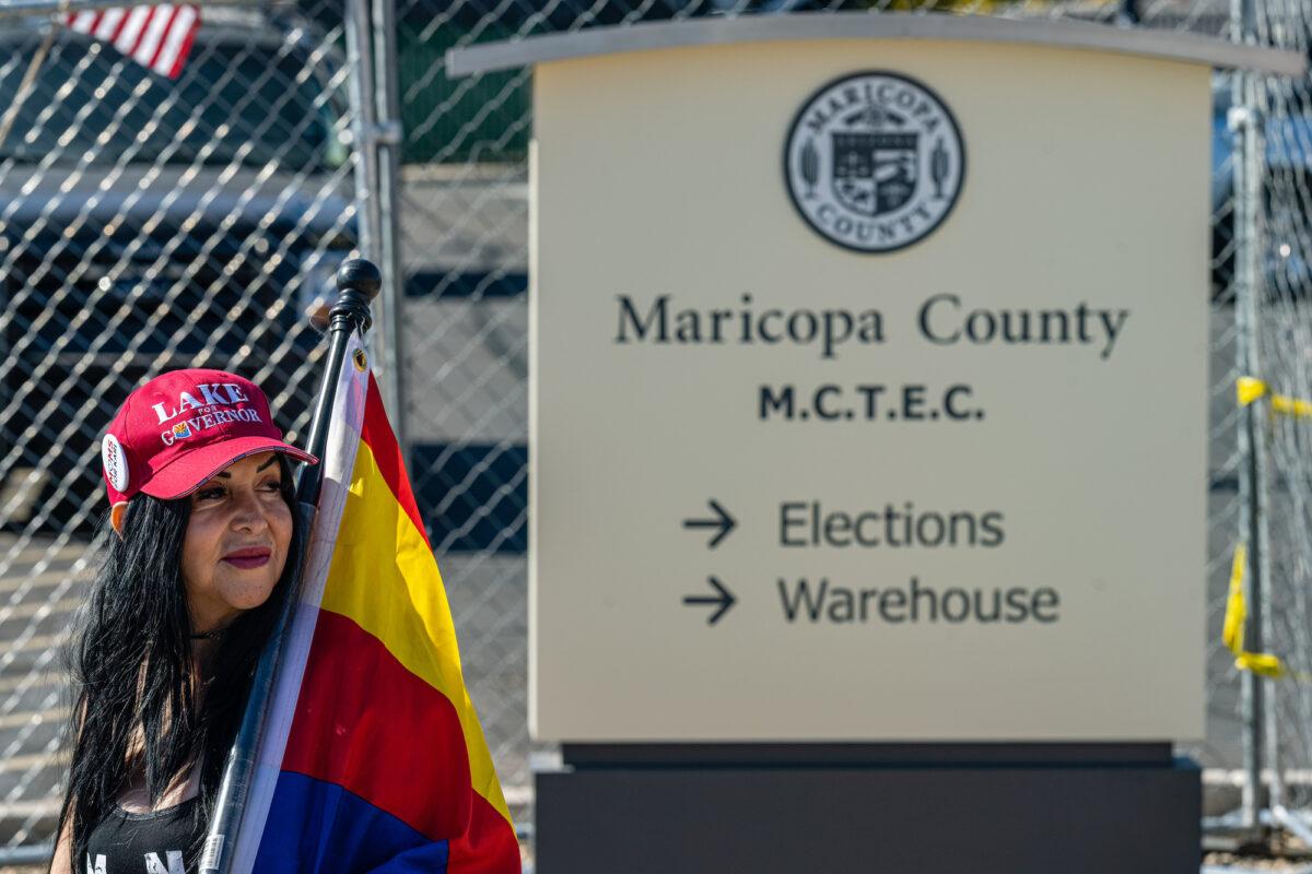 An activist wearing a "Lake for Governor" hat stands on the sidewalk in protest of the election process in front of the Maricopa County Tabulation and Election Center in Phoenix, on Nov. 14, 2022. (Jon Cherry/Getty Images)