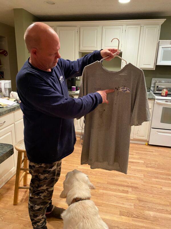 Scott Smith points to the blood stain on the T-shirt he wore on the night of his arrest at his residence in Leesburg, Va., on Dec. 10, 2021. He hasn't washed the T-shirt since his arrest at a Loudoun County school board meeting on June 22, 2021. (Terri Wu/The Epoch Times)