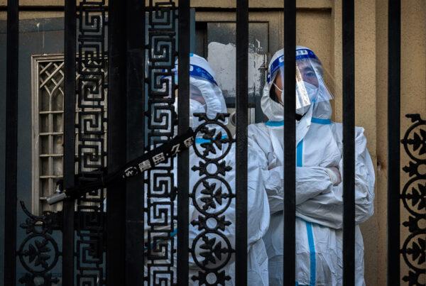 Epidemic control workers wear protective suits to prevent the spread of COVID-19 as they stand guard behind the locked gate of an apartment building in the Central Business District in Beijing on Nov. 26, 2022. (Kevin Frayer/Getty Images)